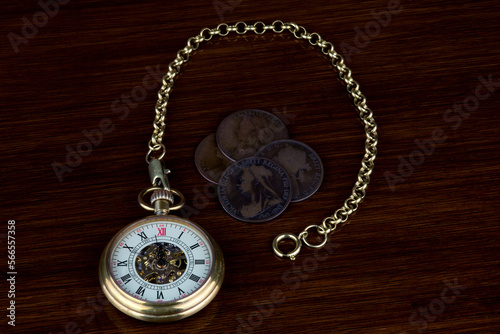 Retro Pocket Watch and Chain with Old Victorian Pennies on a Polished Wooden Surface