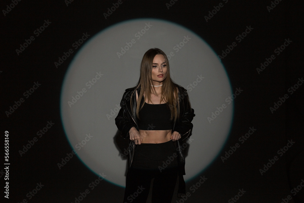 Fashionable young beautiful woman with black casual trendy outfit with top and leather black jacket on a dark background in studio