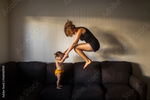 Playful mom jumping on large couch holding hands with her child photo