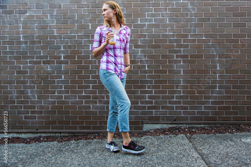 Young woman walking down sidewalk with drink and looking over shoulder, Seattle, Washington State, USA photo