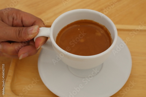 Hand holding espresso coffee in white ceramic cup on wooden table background. 