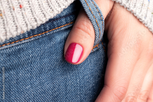 Female hand with beautiful manicure - viva magenta, pink nails on jeans denim textile, closeup thumb finger