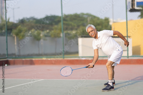 Senior man playing badminton outdoor at badminton court. Concept of active lifestyle being on pension