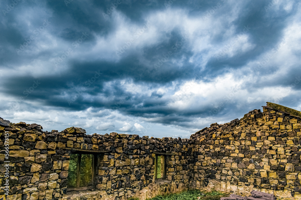 Ancient damaged stone house wall with dramatic clouds running behind.