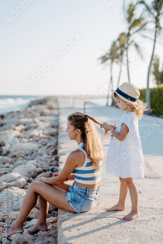 Little girl making hairstyle her mother, enjoying summer time at sea. © Halfpoint