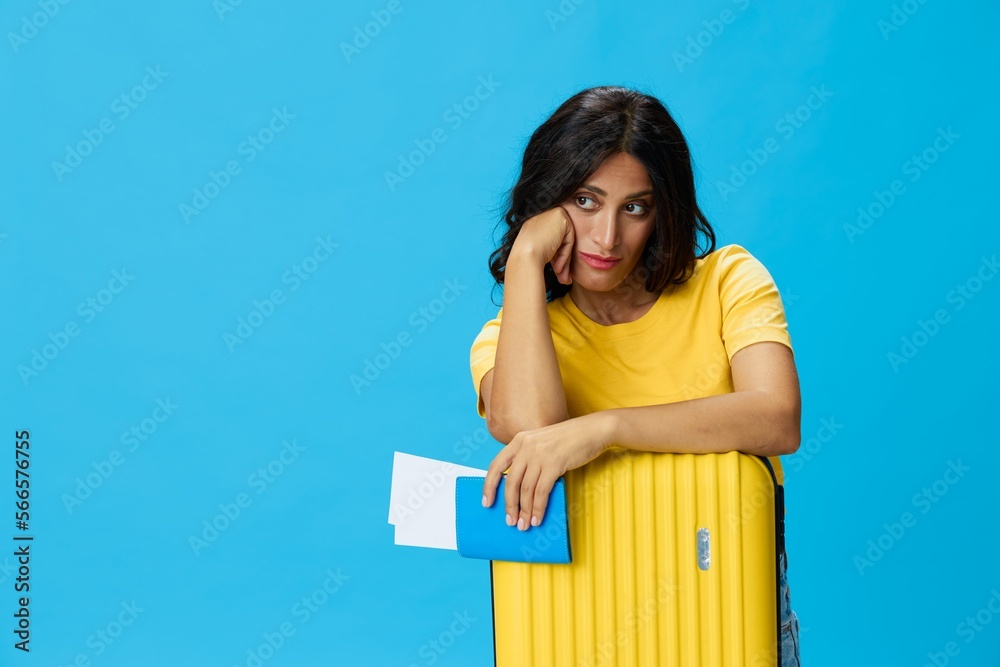 Travel woman with yellow suitcase, passport and ticket in hand, paper plane, in yellow T-shirt on blue background, happiness from travel, glasses, copy space