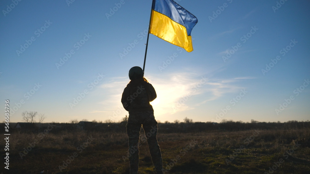 Soldier of ukrainian army holding waving flag of Ukraine. Woman in military uniform and helmet lifted up yellow-blue flag. Victory against russian aggression. Invasion resistance concept. Slow motion