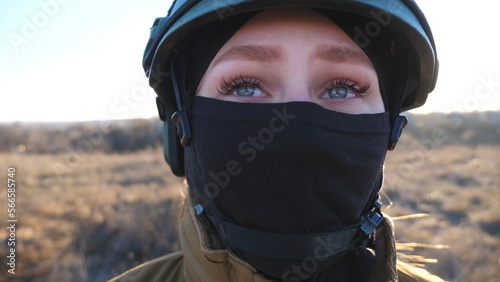 Young female ukrainian soldier in military uniform and helmet looks around her. Woman watching at camera with hope in eyes. Victory against Russian aggression. Invasion resistance concept. Close up