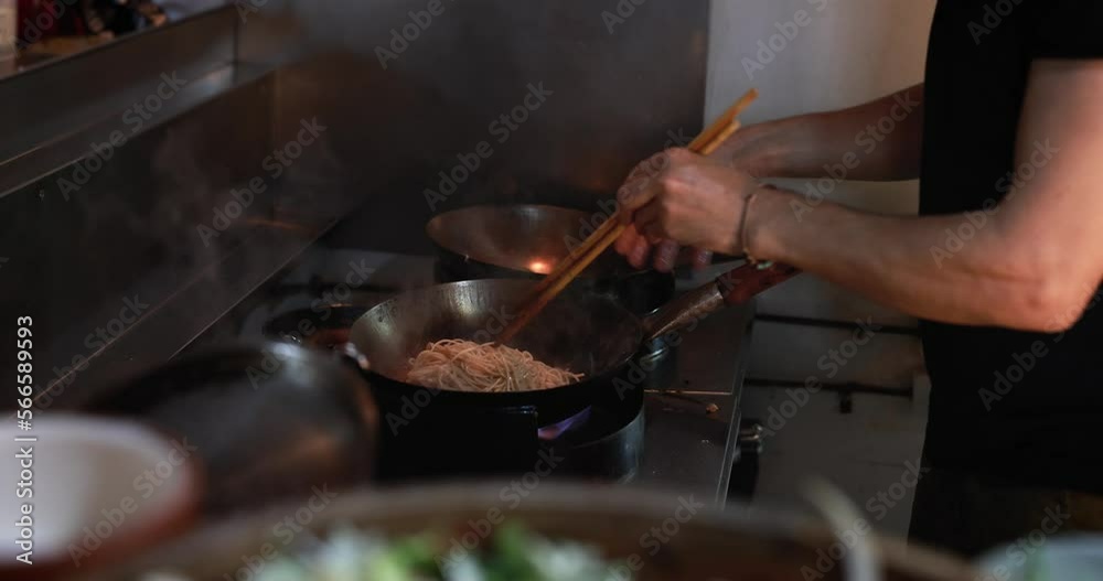 Chef using chopsticks while cooking asias dish using the metal wok Chef using chopsticks while cooking asias dish using the metal wok