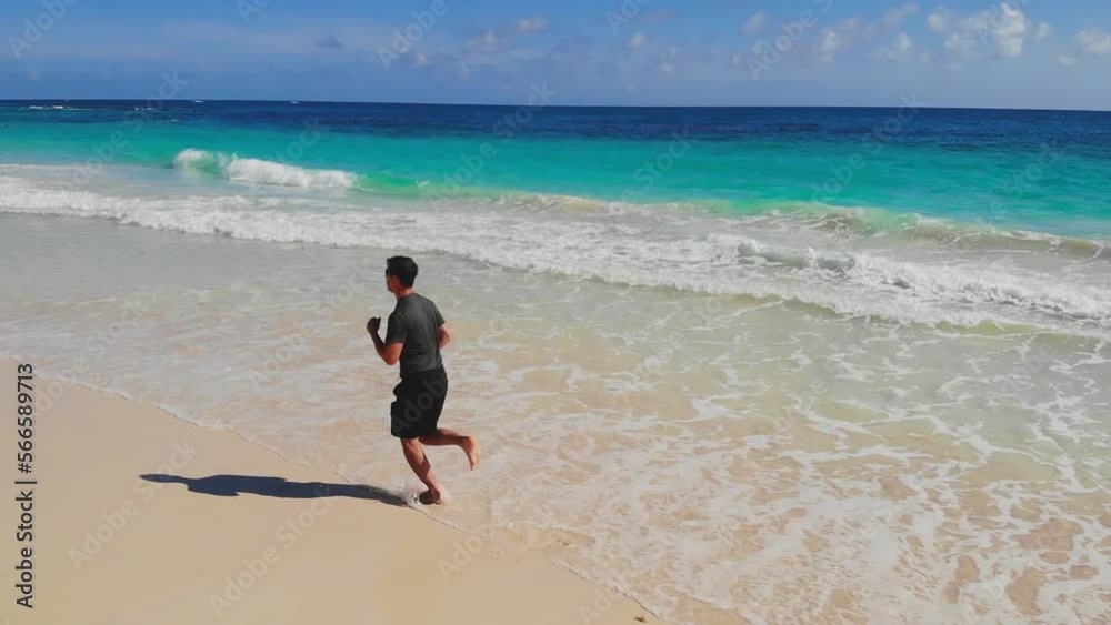 Fitness man running jog on morning at sea. Adult slim, athletic, fit man runs barefoot along coast of sea on sand. Sports jogging on vacation along coastline of ocean. Healthy lifestyle in clean air. Fitness man running jog on morning at sea. Adult slim, athletic, fit man runs barefoot along coast of sea on sand. Sports jogging on vacation along coastline of ocean. Healthy lifestyle in clean air.