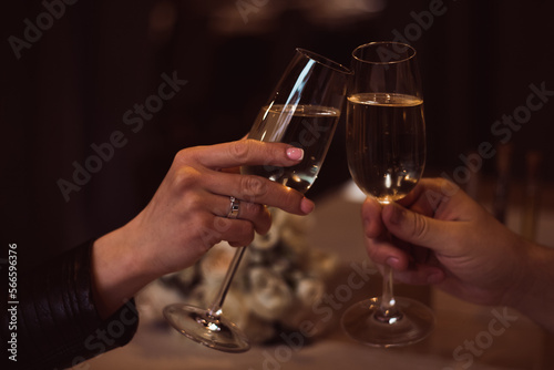 Two glasses with sparkling champagne wine in hands, concept for holiday, bokeh, in a restaurant. Romantic dinner. Man and woman are holding glasses of champagne. Concept for Valentine's day or date. © Dubnytskaya Photo