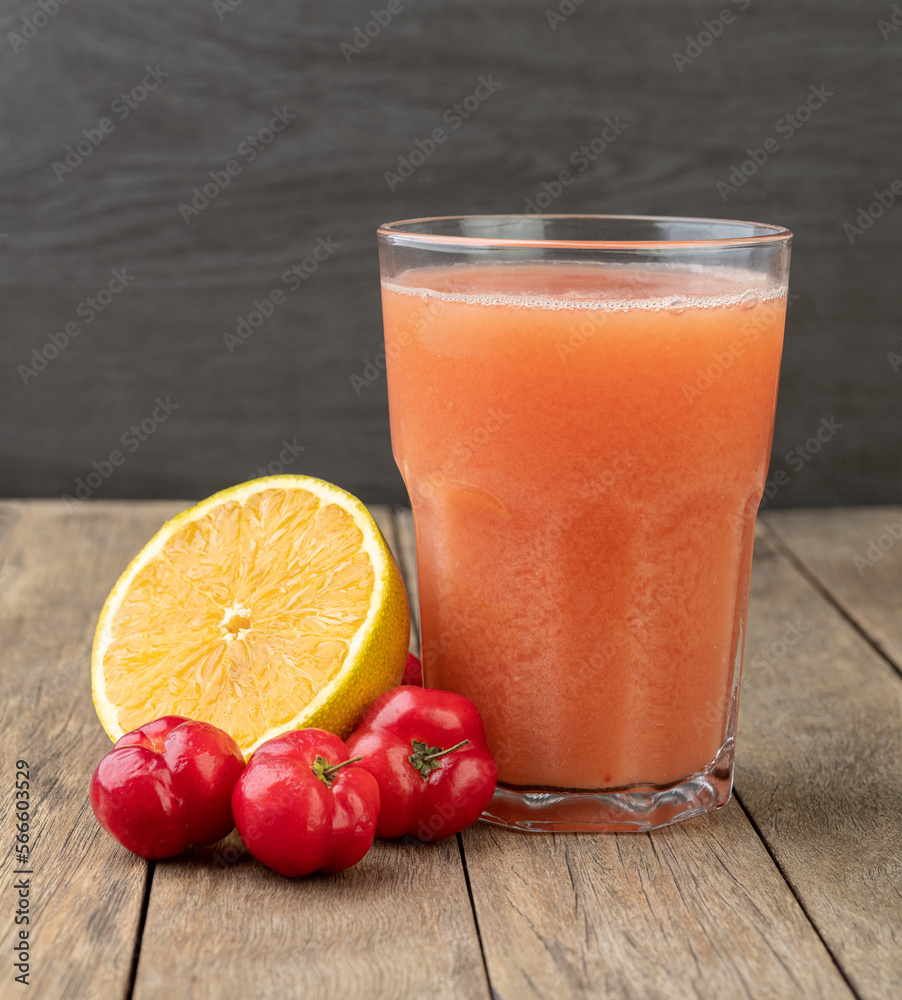 Acerolas or Barbados Cherries and orange juice with fruits over wooden table Acerolas or Barbados Cherries and orange juice with fruits over wooden table