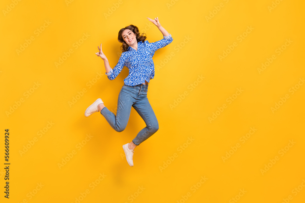 Full size portrait of excited energetic girl jumping demonstrate v-sign empty space isolated on yellow color background Full size portrait of excited energetic girl jumping demonstrate v-sign empty space isolated on yellow color background