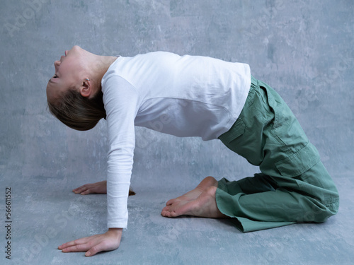 Selective focus portrait of little blond girl exercising by kneeling on floor and stretching backwards