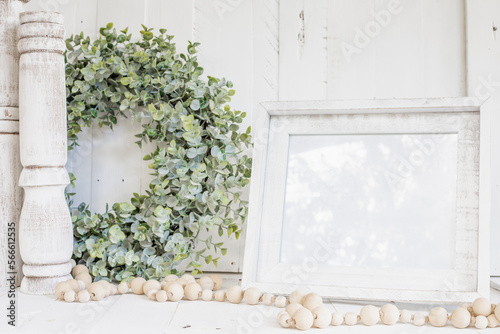 White picture frame blank mock-up with white background , natural wooden beads and green wreath, farmhouse styled