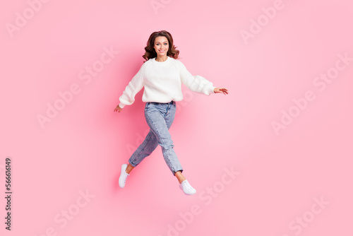 Full length photo of cute shiny woman dressed white pullover walking empty space jumping high isolated pink color background