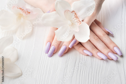 Girl s hands with delicate purple manicure and orchid flowers