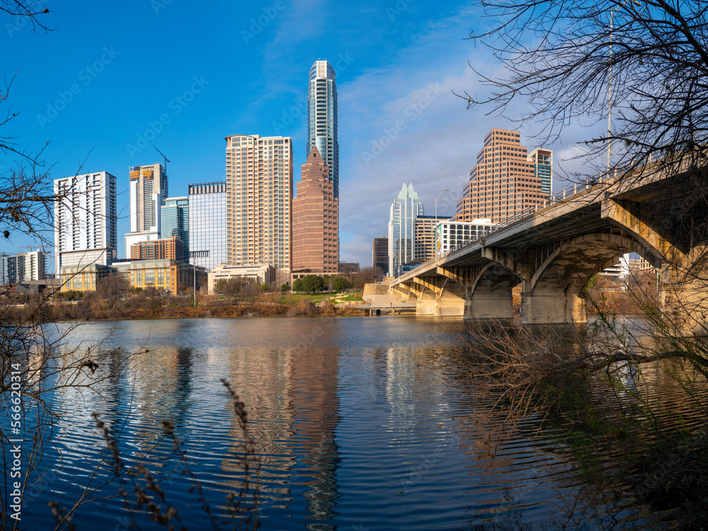 Naklejka premium Vibrant Austin Texas city panoramic skyline behind trees, modern buildings, reflections on the Lady Bird Lake in Colorado River, and the Congress Avenue Bridge over the boardwalk