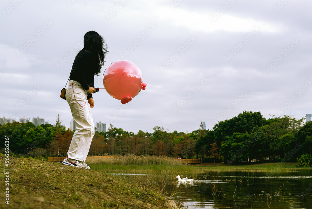Obraz premium a woman stands by lake with a pink balloon