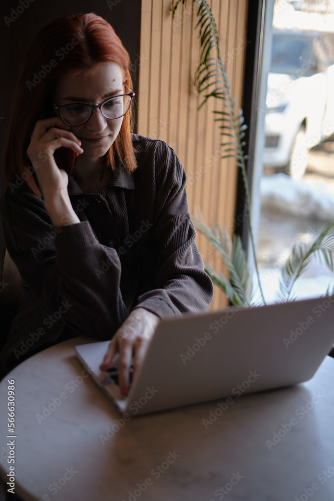 a red-haired freelance woman with glasses works remotely on a laptop in a cafe.x a red-haired freelance woman with glasses works remotely on a laptop in a cafe.x