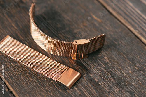 Close up of steel rose watch strap laying on the dark brown rustic wooden table.
