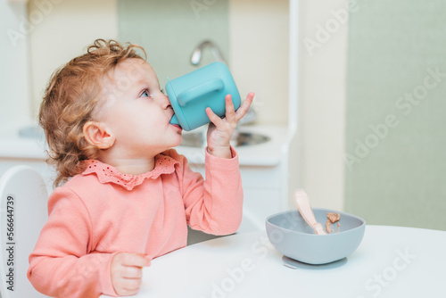 Little child drinking water from a plastic cup at home