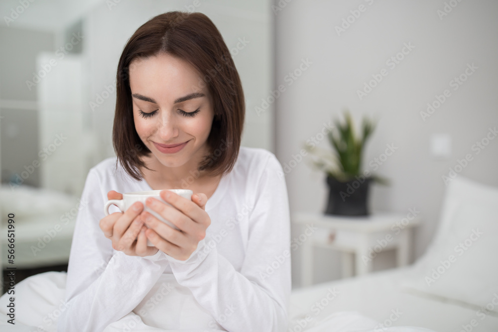 Closeup of smiling young woman enjoying morning coffee in bed Closeup of smiling young woman enjoying morning coffee in bed
