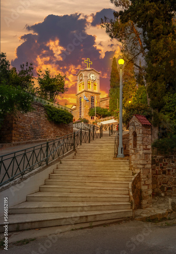 Steps to Saints Anargyri Holy Orthodox Church with a clock and a cross on island Evia in Greece at sunset photo