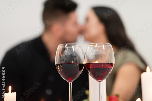 Selective focus on glasses with red wine over kissing couple