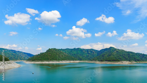 Dam view with emerald green water  There are green mountains  and bright sky © Eakkarach