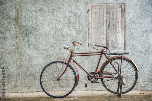 Vintage bicycle on old rustic dirty wall house, many stain on wood wall. Classic bike old bicycle on decay brick wall retro style. Cement loft partition and window background. © BESTIMAGE