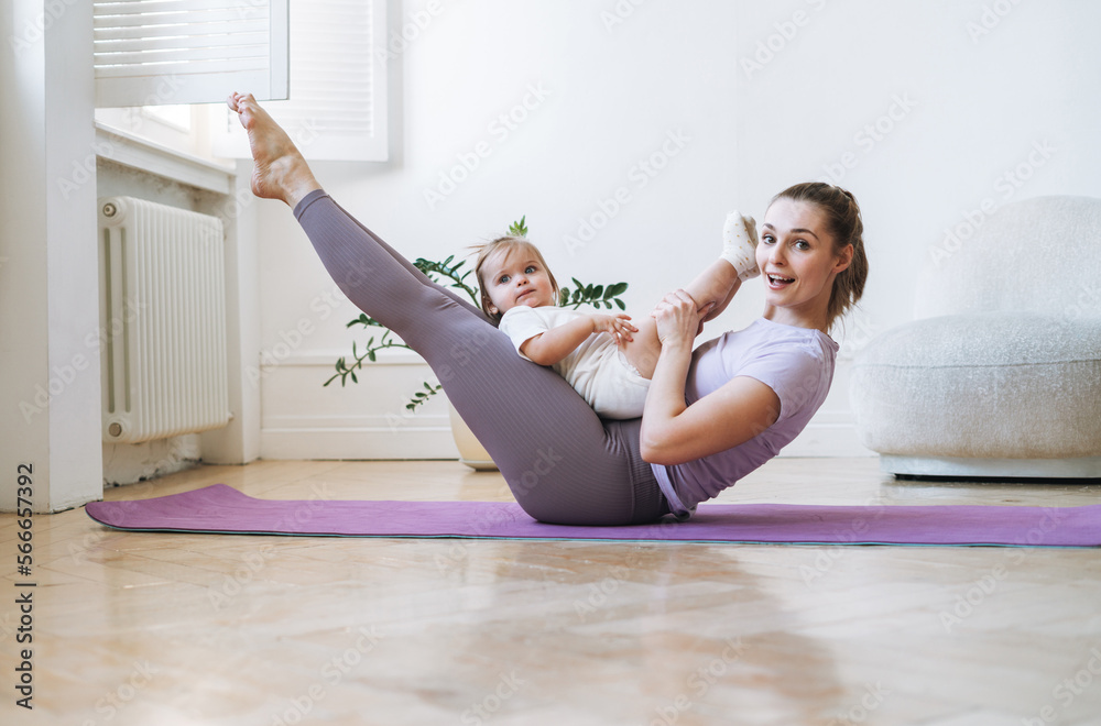 Young woman fit mom with baby girl doing fitness on mat at home