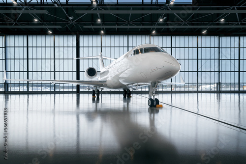 Private jet airplane at the huge white hangar waiting for maintenance and repair jobs. Expensive and luxury trip is waiting after a passengers. Business jet prepared for departure