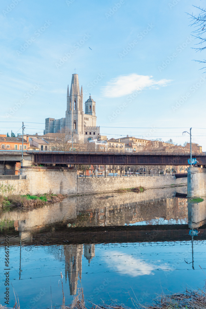 Puente para cruzar por encima del río caminando  y entrar a la ciudad de Gerona bajo un día soleado y cálido con el reflejo de la catedral en el río.