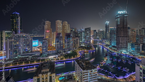 Panorama showing Dubai Marina with several boat and yachts parked in harbor and skyscrapers around canal aerial night .