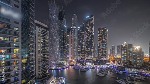 Panorama showing Dubai marina tallest skyscrapers and yachts in harbor aerial night .