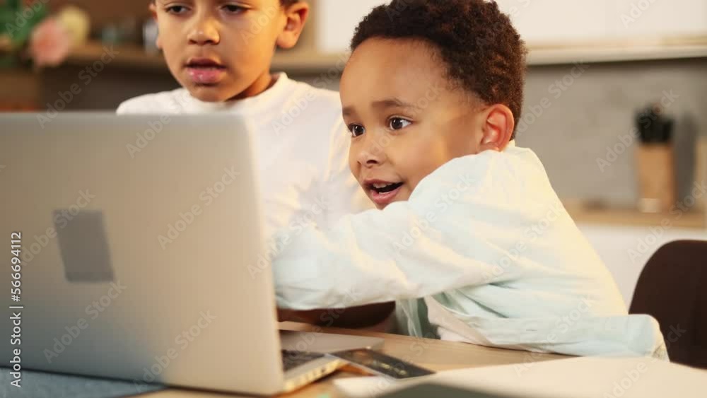 Cute primary school boys kids studying using laptop computer together at home kitchen Adorable african american brothers doing homework writing exercise in notebook indoors Distance online education Cute primary school boys kids studying using laptop computer together at home kitchen Adorable african american brothers doing homework writing exercise in notebook indoors Distance online education