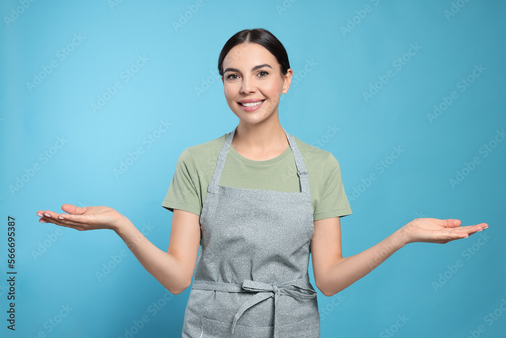 Young woman in grey apron on light blue background, Young woman in grey apron on light blue background,