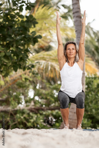 a fit, slender middle-aged female yoga instructor performs asanas, conducts group training outdoors in the shade of palm trees. The concept of fitness, sports and healthy lifestyle