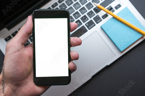 Man Holding Smartphone with blank screen, on the background modern laptop.