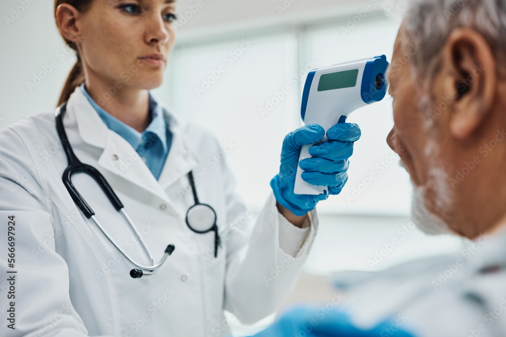 Close up of doctor using infrared thermometer while measuring temperature of her senior patient. Close up of doctor using infrared thermometer while measuring temperature of her senior patient.