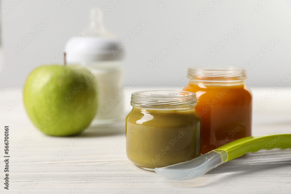 Jars with healthy baby food and spoon on white wooden table. Space for text