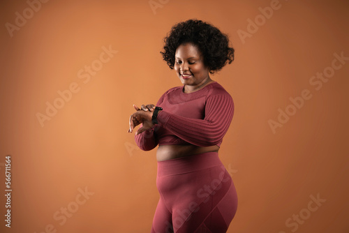 Body positive curvy black girl wearing sportswear in studio doing yoga and working out with sports accessories looking at smart watch