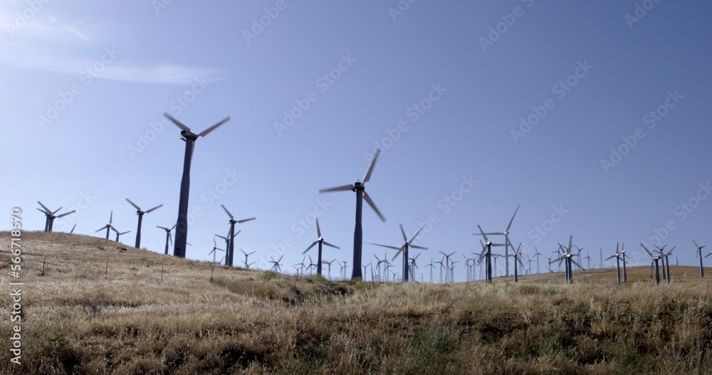 Wide view of smaller wind turbines back lit and silhouetted on a rural hillside in the Tehachapi Mountains in California. Wide view of smaller wind turbines back lit and silhouetted on a rural hillside in the Tehachapi Mountains in California.
