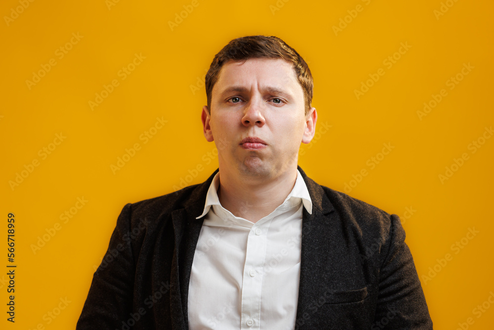 Close up of sad businessman wearing suit looking at camera on yellow studio background Close up of sad businessman wearing suit looking at camera on yellow studio background