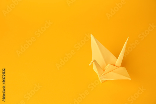 Origami art. Beautiful light yellow paper crane on orange background  space for text