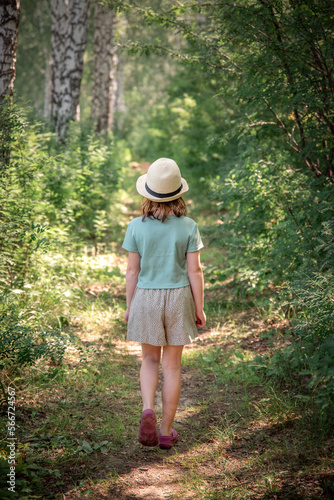 a cute girl in a straw hat walks along a path in the woods in the summer © iloli