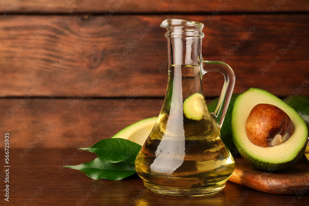 Glass jug of cooking oil and fresh avocados on wooden table, space for text Glass jug of cooking oil and fresh avocados on wooden table, space for text