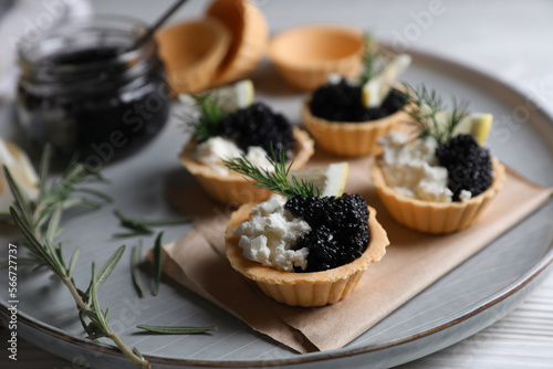Delicious tartlets with black caviar, cream cheese and lemon served on white wooden table, closeup