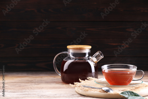 Aromatic hot tea in glass cup and teapot on wooden table. Space for text